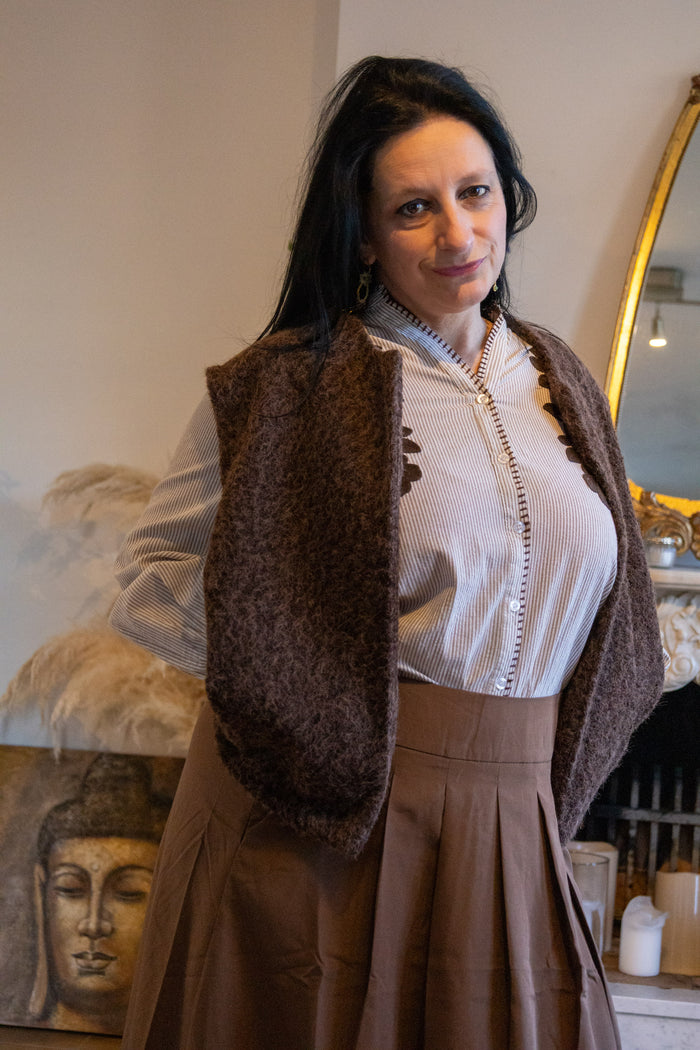 Dame in een bruin vest met een gestreept hemd en een bruine rok in een sfeervolle omgeving.