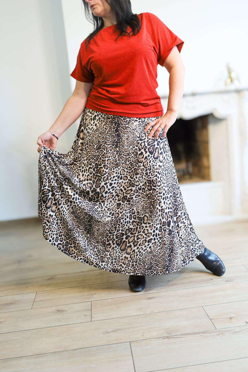 Vrouw draagt een lange rok met luipaardprint van Terra di Siena, gecombineerd met een felrode top en zwarte laarzen.