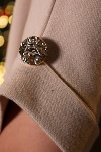 Beige jas met een opvallende metalen knoop, trendy en elegant detail.