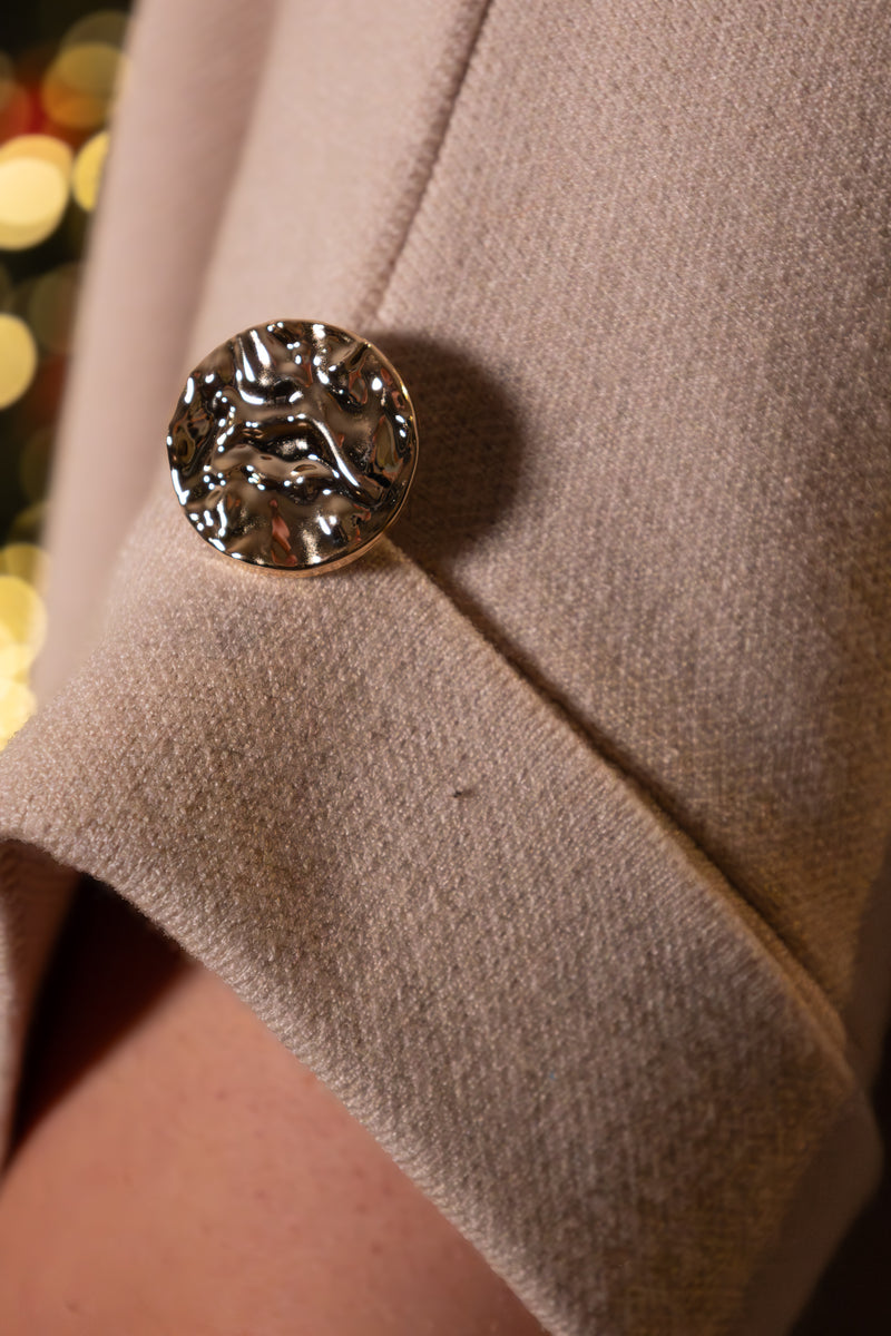 Beige jas met een opvallende metalen knoop, trendy en elegant detail.