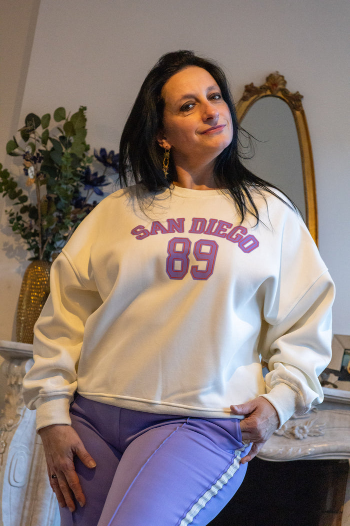 Modieuze witte sweatshirt met 'San Diego 89' opdruk, gecombineerd met paarse sportlegging.