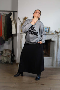 Vrouw in grijze oversized sweater met 'Mrs. Cool'-print, zwarte rok en hoge laarzen, stijlvol en casual. She & Me damesmode.