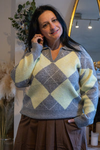 Vrouw in een lichtgrijze trui met geel en grijs ruitpatroon, donkere rok, casual stijl.