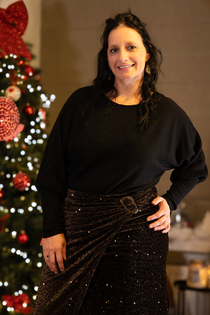 Zwarte oversized trui met glinsteringen, gecombineerd met een glanzende zwarte rok.