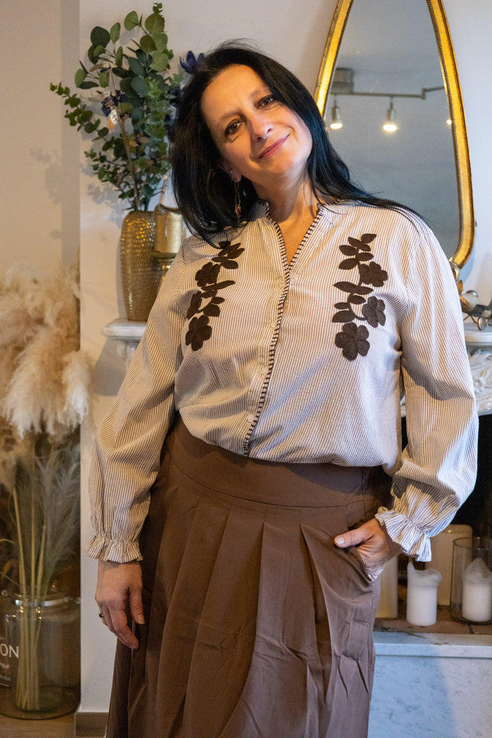Strepen blouse met bloemen borduring, gecombineerd met een bruine plooienrok voor een trendy look.