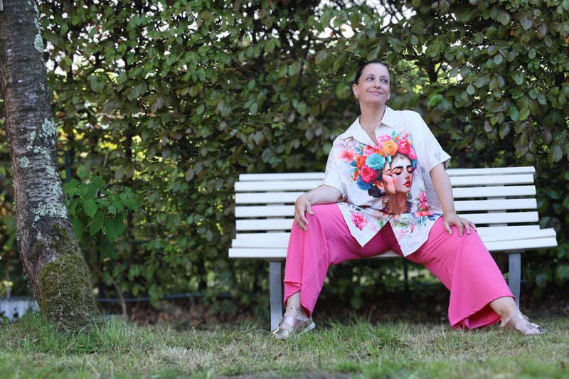 Witte oversized blouse met kleurrijk bloemenportret en artistieke details. Een gedurfde en vrouwelijke statement piece.