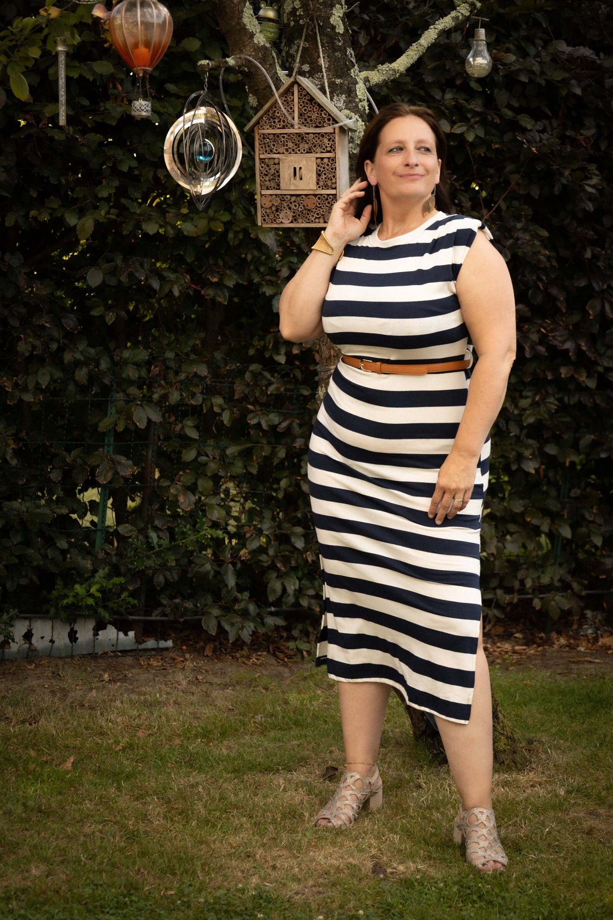Vrouw in een gestreepte Terra Di Siena jurk marineblauw, poseert buiten met een elegante uitstraling.