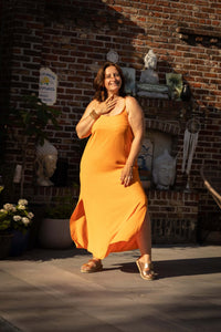 Vrouw in oranje strapless maxi-jurk met zijsplit, perfect voor zomerse dagen en vakanties.