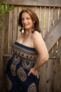 Vrouw in strapless navy jumpsuit met elegante bohemian print, poseert voor houten schutting.