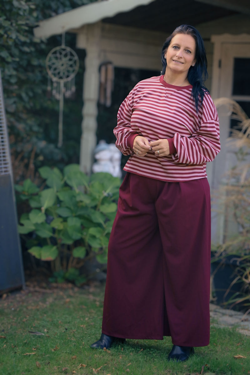 Vrouw draagt wijde bordeauxrode Dolci Giorni pantalon – elegante damesbroek bij She&Me Duffel.