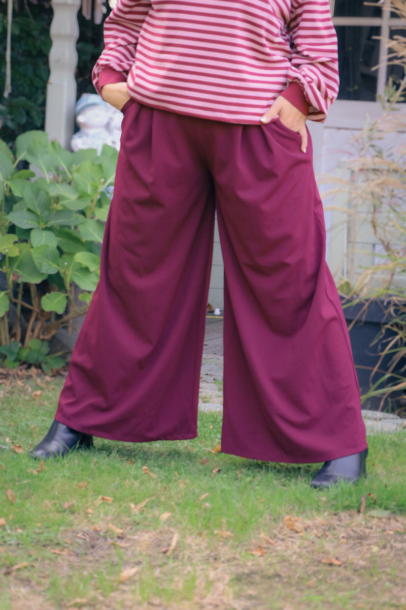 Vrouw draagt wijde bordeauxrode Dolci Giorni pantalon – elegante damesbroek bij She&Me Duffel.