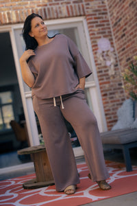 Vrouw poseert in taupe kleurige  Dolci Giorni set met losse top en broek – comfortabele damesmode bij She&Me Duffel.