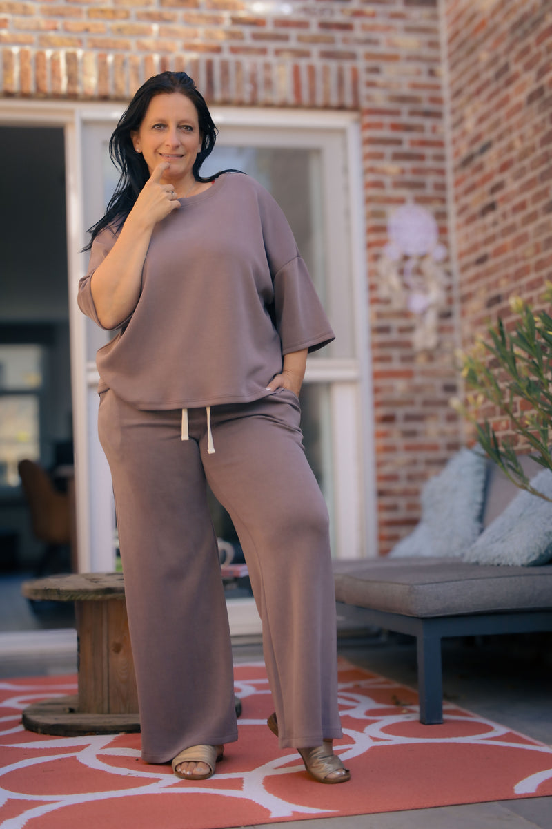 Vrouw poseert in taupe kleurige  Dolci Giorni set met losse top en broek – comfortabele damesmode bij She&Me Duffel.