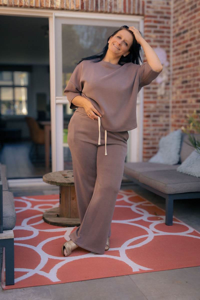 Vrouw poseert in taupe kleurige  Dolci Giorni set met losse top en broek – comfortabele damesmode bij She&Me Duffel.
