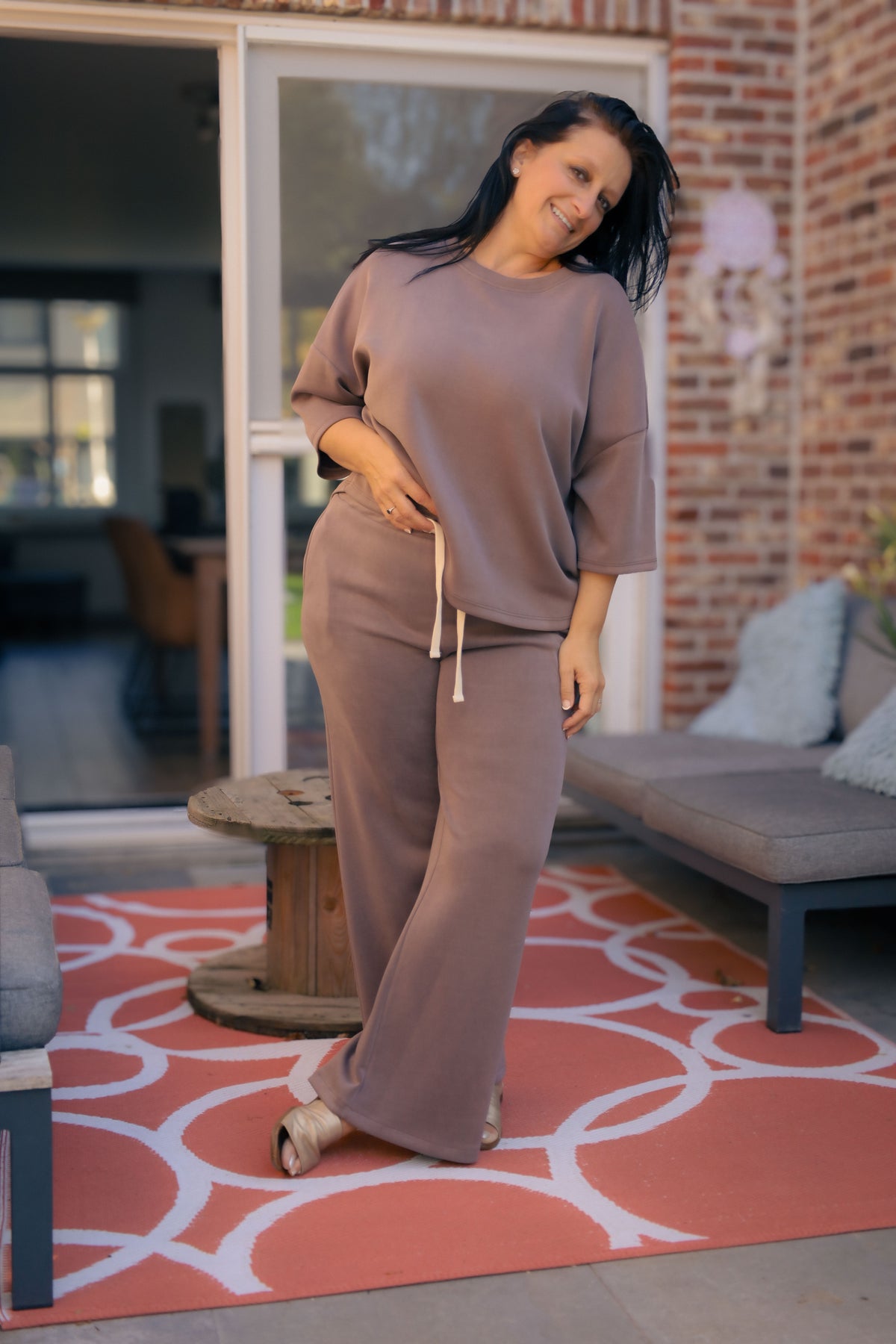 Vrouw poseert in taupe kleurige  Dolci Giorni set met losse top en broek – comfortabele damesmode bij She&Me Duffel.