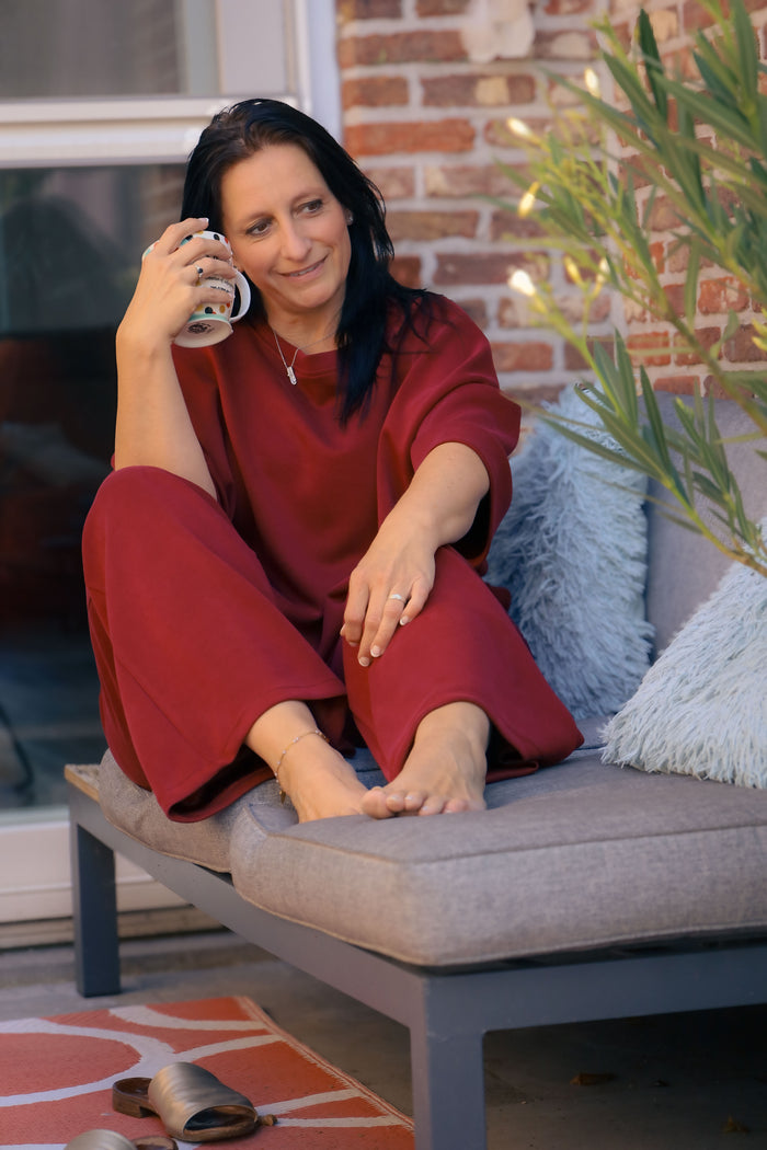 Vrouw poseert in bordeauxrode Dolci Giorni set met losse top en broek – comfortabele damesmode bij She&Me Duffel.