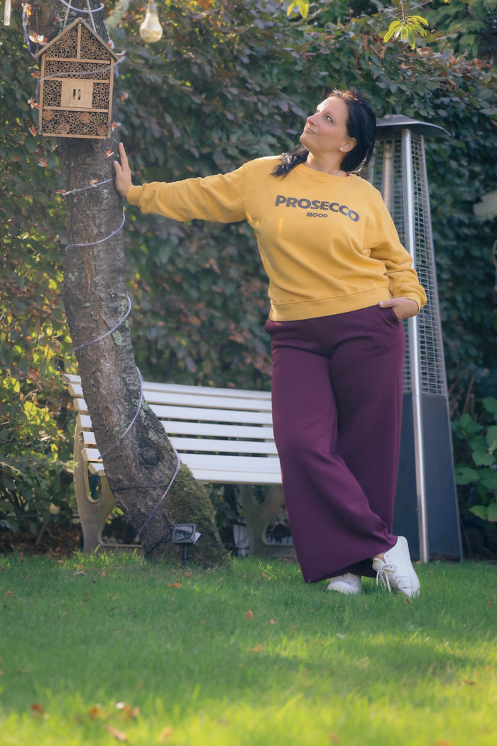 Vrouw draagt mosterdgele Dolci Giorni sweater met ‘Prosecco Mood’-print – comfortabele damesmode bij She&Me Duffel.