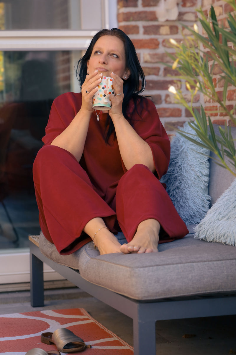 Vrouw poseert in bordeauxrode Dolci Giorni set met losse top en broek – comfortabele damesmode bij She&Me Duffel.