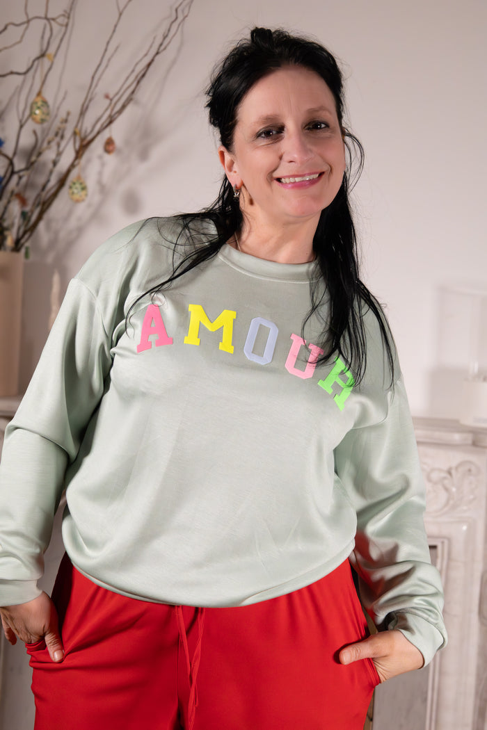 Maglia Amore Dolce – mint sweater met print worn by a smiling woman, featuring colorful 'Amour' letters.