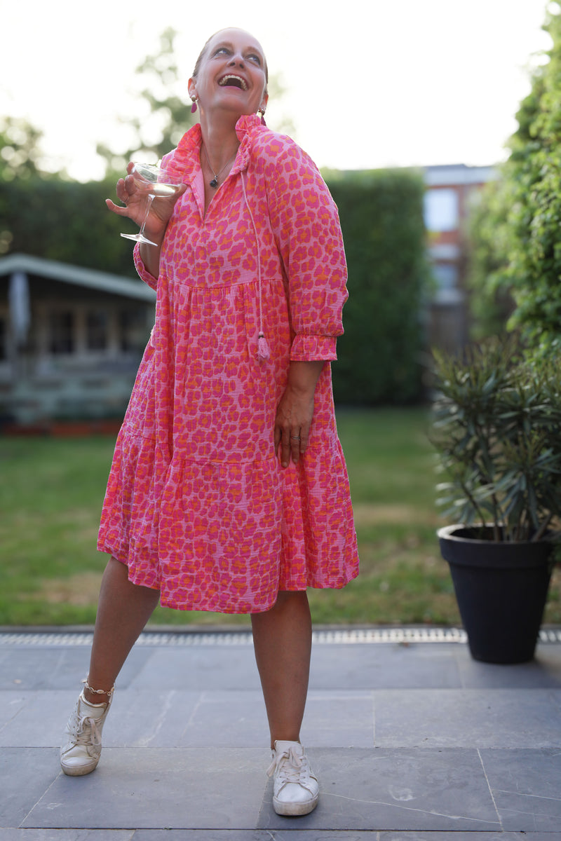 Maxi-jurk met levendige roze luipaardprint, lichte crinkle-stof en speelse rufflekraag. Een echte zomerstatement!