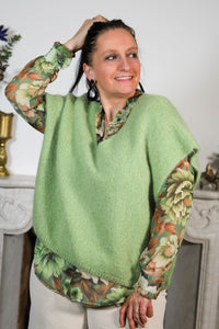 Vrouw draagt een groene mouwloze trui over een bloemenblouse, gecombineerd met een lichte broek voor een frisse en stijlvolle look