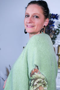 Vrouw draagt een groene mouwloze trui over een bloemenblouse, gecombineerd met een lichte broek voor een frisse en stijlvolle look