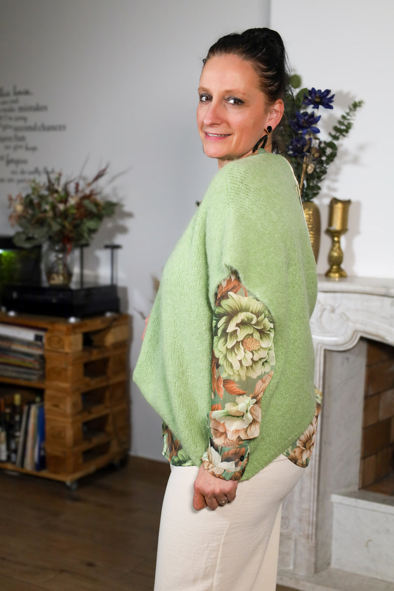 Vrouw draagt een transparante blouse met bloemenprint in groene en beige tinten, gecombineerd met een subtiele kraag en natuurlijke uitstraling