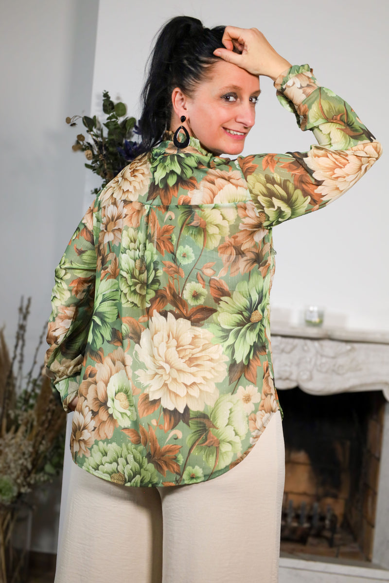 Vrouw draagt een transparante blouse met bloemenprint in groene en beige tinten, gecombineerd met een subtiele kraag en natuurlijke uitstraling