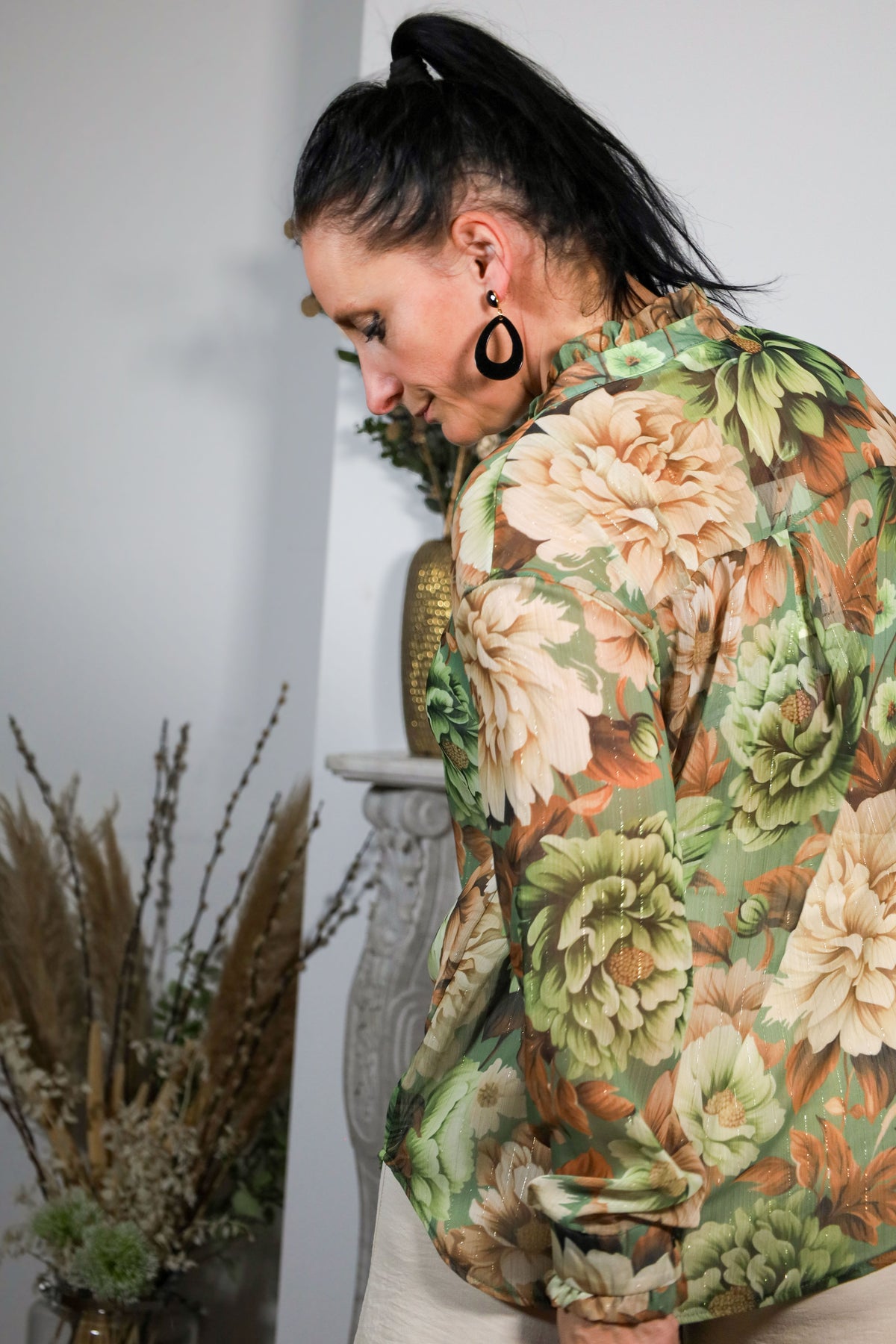 Vrouw draagt een transparante blouse met bloemenprint in groene en beige tinten, gecombineerd met een subtiele kraag en natuurlijke uitstraling