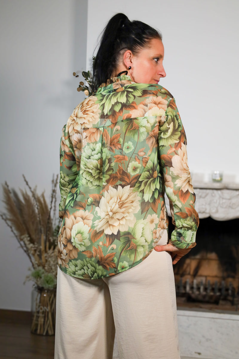 Vrouw draagt een transparante blouse met bloemenprint in groene en beige tinten, gecombineerd met een subtiele kraag en natuurlijke uitstraling