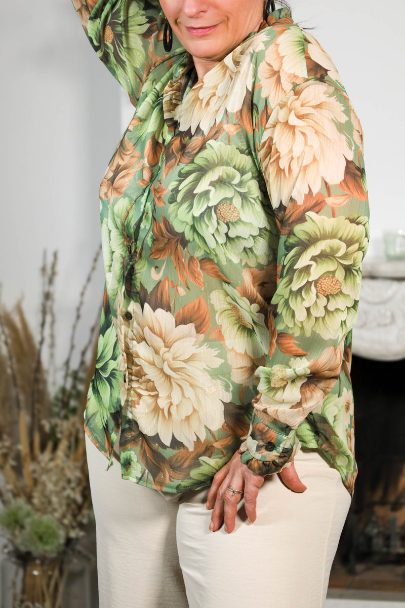 Vrouw draagt een transparante blouse met bloemenprint in groene en beige tinten, gecombineerd met een subtiele kraag en natuurlijke uitstraling