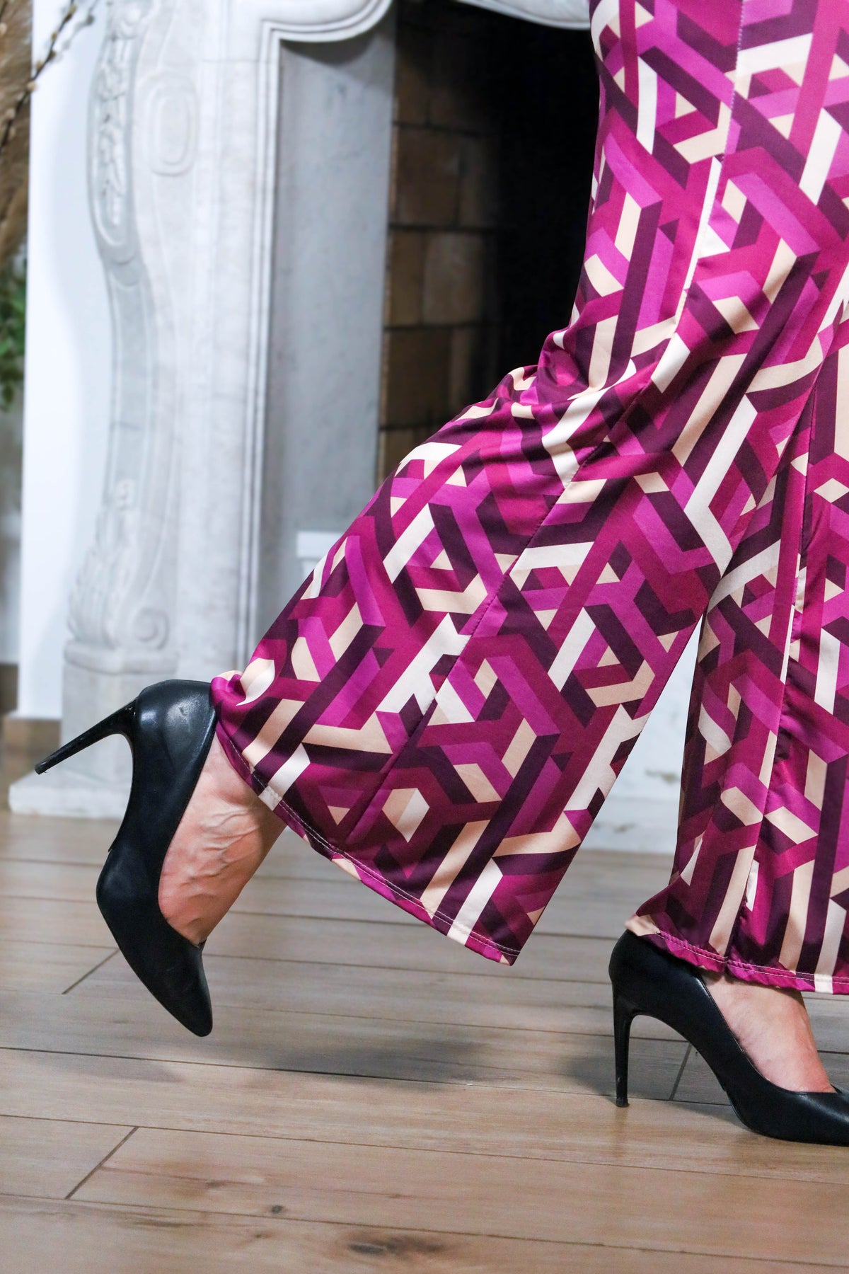 Close-up van een elegante broek met geometrische print in paarse en beige tinten, gedragen met zwarte hakken.