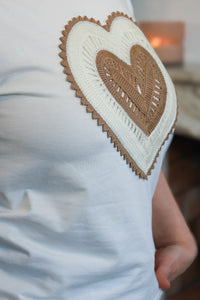 Vrouw draagt een wit T-shirt met een geborduurd hart in beige tinten, gecombineerd met een lichte broek