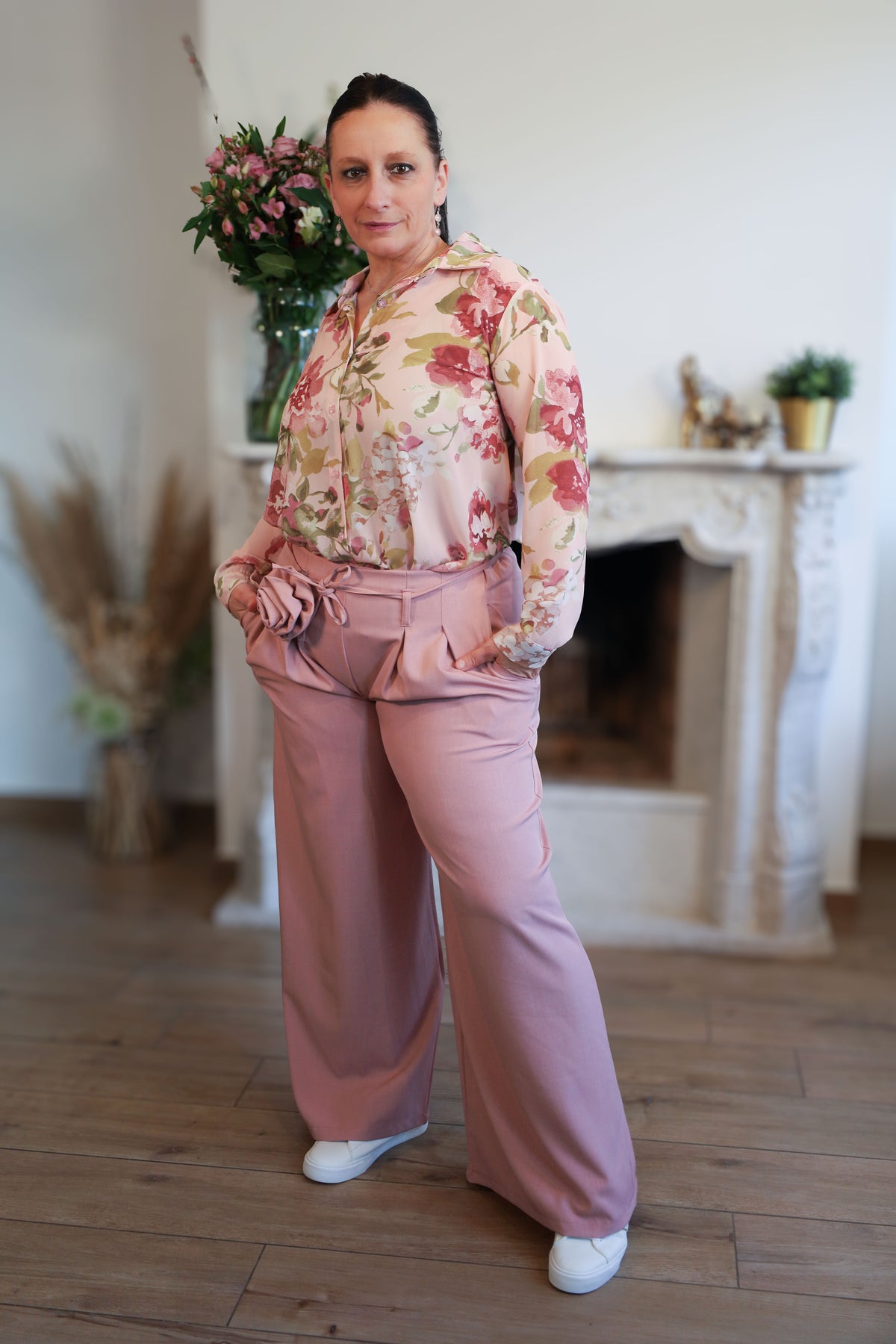 Vrouw draagt een transparante blouse met romantische bloemenprint, gecombineerd met een roze pantalon.