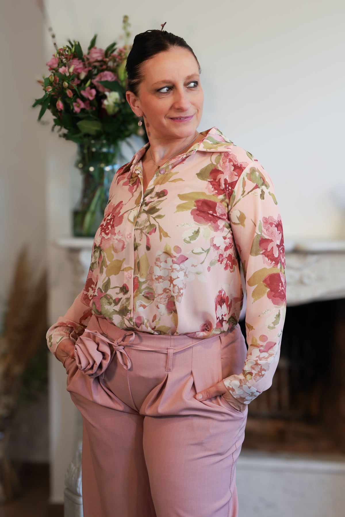 Vrouw draagt een transparante blouse met romantische bloemenprint, gecombineerd met een roze pantalon.