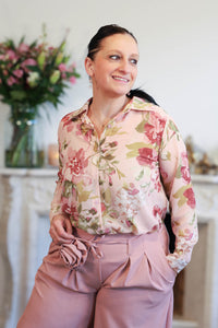 Vrouw draagt een transparante blouse met romantische bloemenprint, gecombineerd met een roze pantalon.