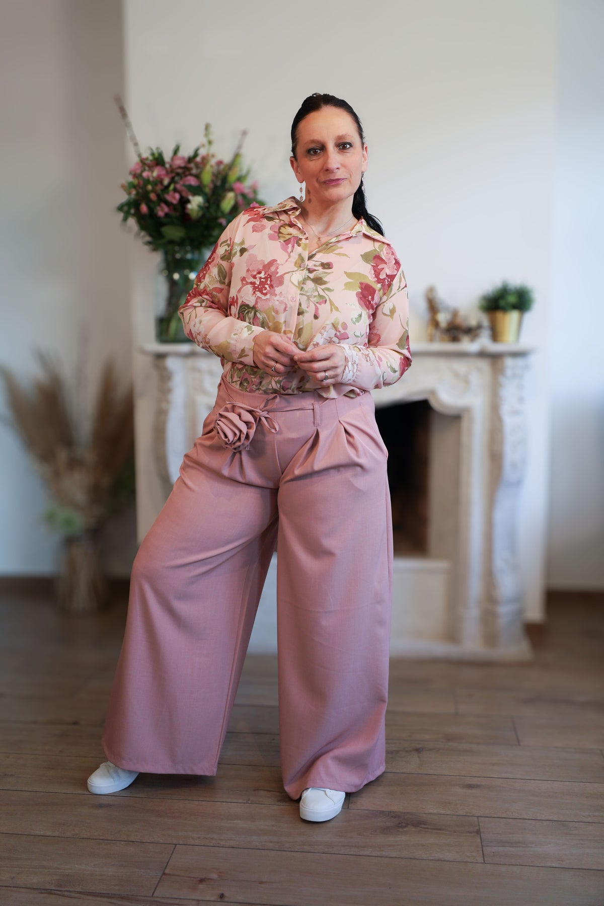 Vrouw draagt een transparante blouse met romantische bloemenprint, gecombineerd met een roze pantalon.