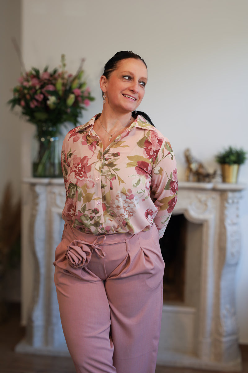 Vrouw draagt een transparante blouse met romantische bloemenprint, gecombineerd met een roze pantalon.