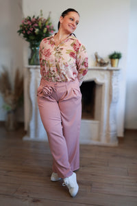 Vrouw draagt een transparante blouse met romantische bloemenprint, gecombineerd met een roze pantalon.