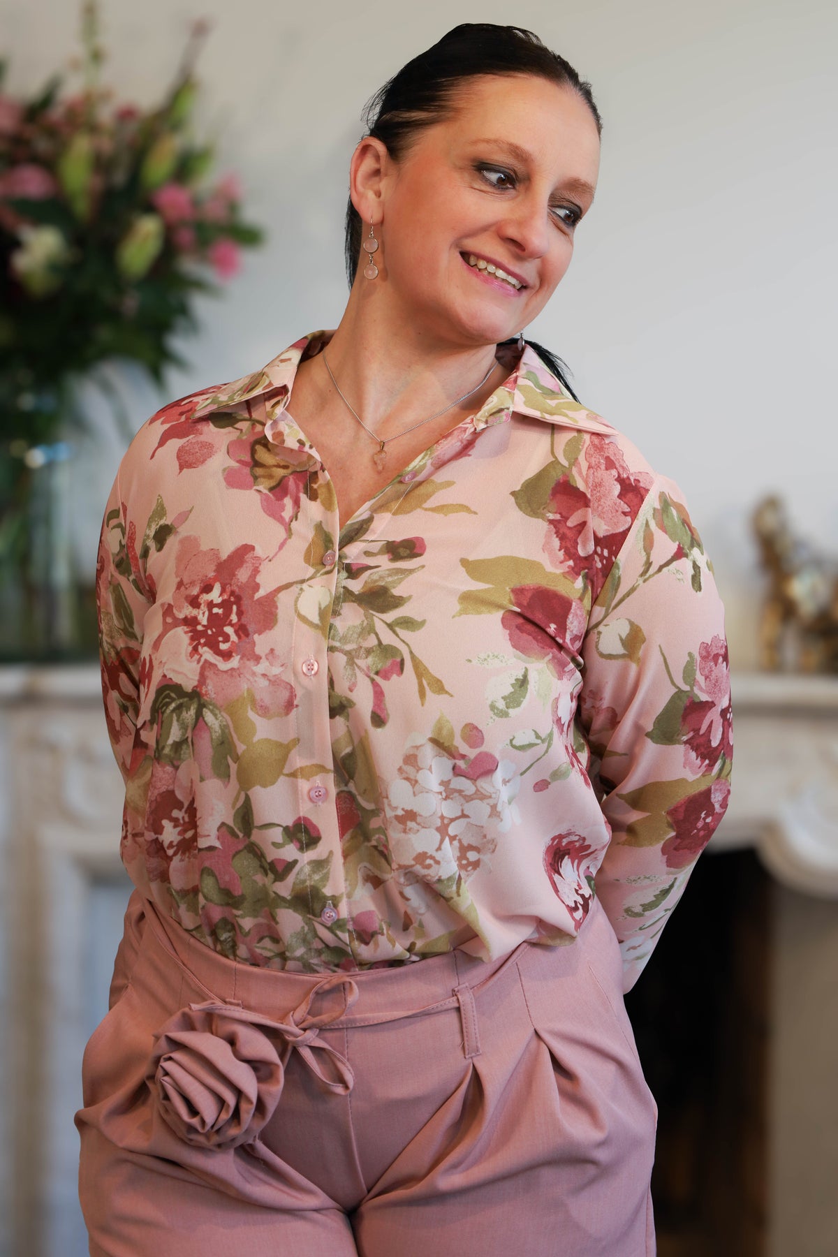 Vrouw draagt een transparante blouse met romantische bloemenprint, gecombineerd met een roze pantalon.