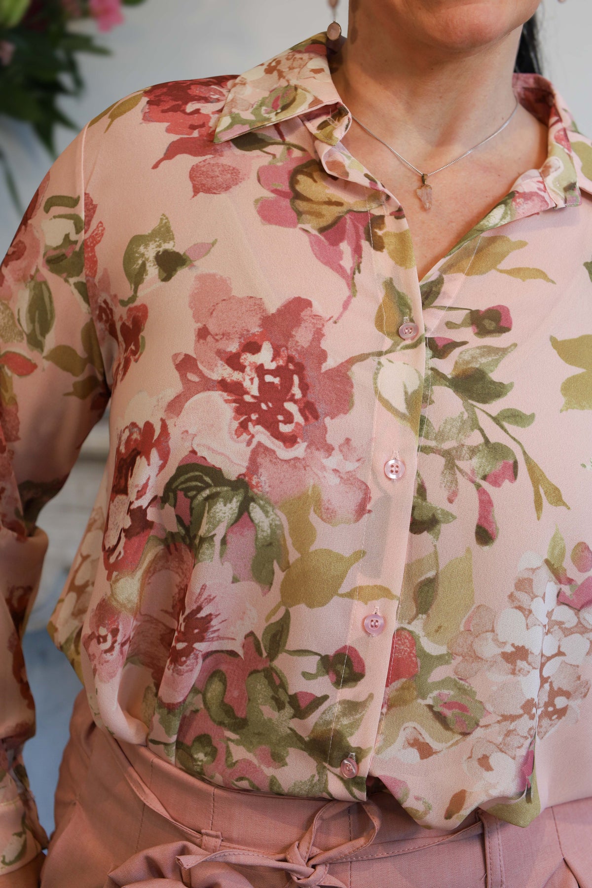 Vrouw draagt een transparante blouse met romantische bloemenprint, gecombineerd met een roze pantalon.