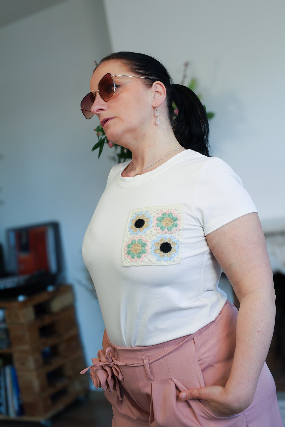 Vrouw draagt een wit T-shirt met een geborduurde bloemenpatch op de borst, gecombineerd met een roze wijde broek