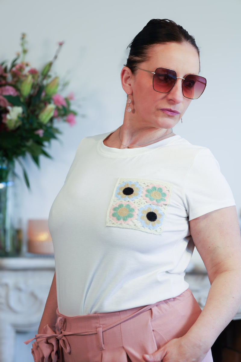 Vrouw draagt een wit T-shirt met een geborduurde bloemenpatch op de borst, gecombineerd met een roze wijde broek