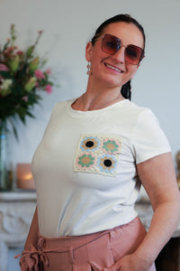 Vrouw draagt een wit T-shirt met een geborduurde bloemenpatch op de borst, gecombineerd met een roze wijde broek