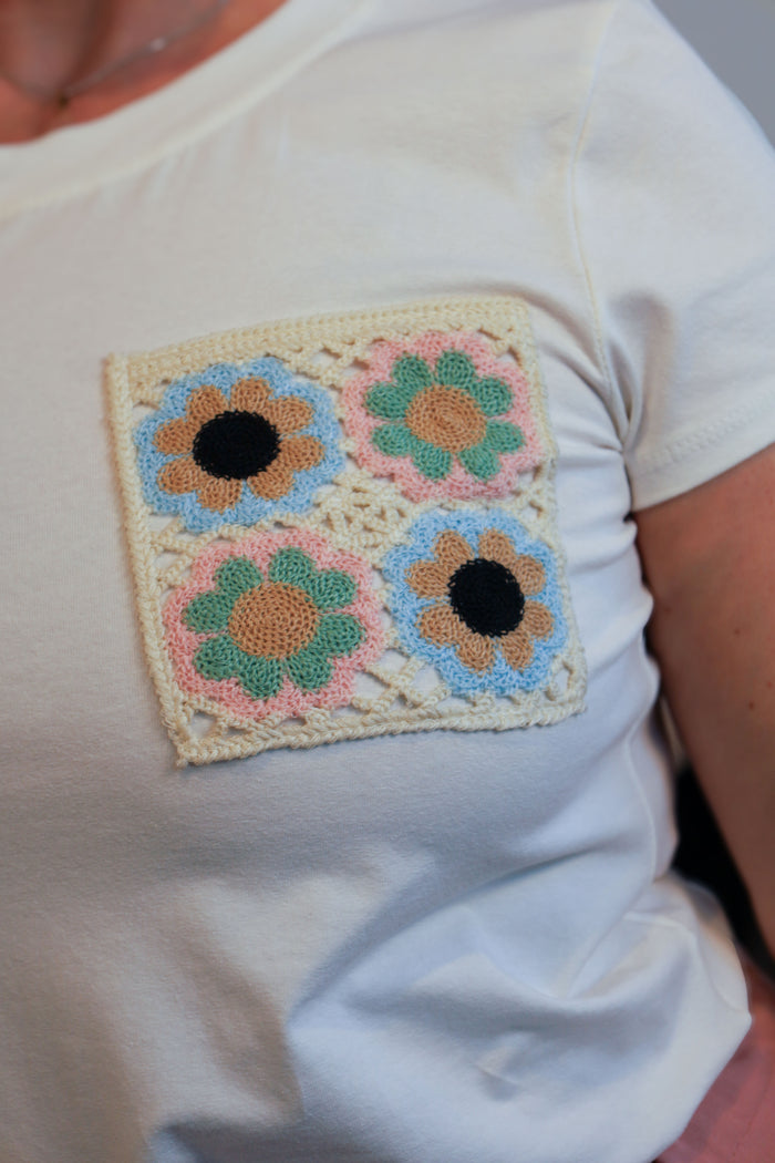 Vrouw draagt een wit T-shirt met een geborduurde bloemenpatch op de borst, gecombineerd met een roze wijde broek