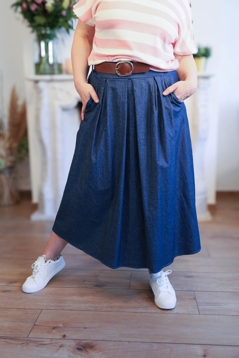 Vrouw draagt een donkerblauwe midi-rok in denimlook, gecombineerd met een roze-wit gestreept T-shirt, riem en sneakers