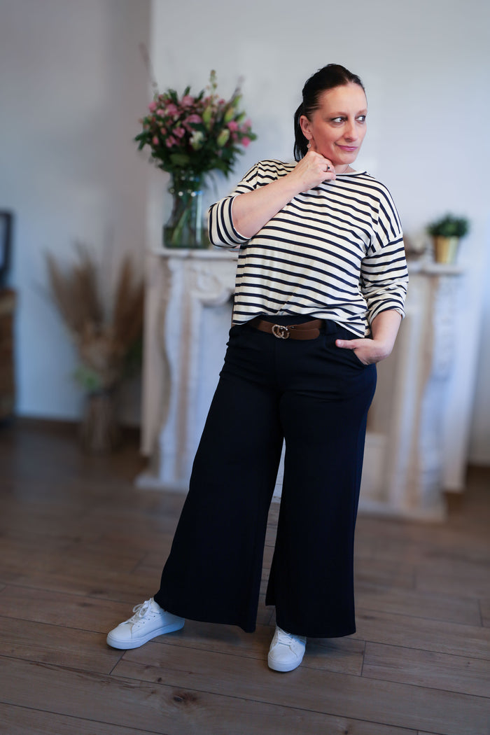 Vrouw draagt een navy-wit gestreepte top met 3/4 mouwen en boothals, gecombineerd met een zwarte pantalon en riem.