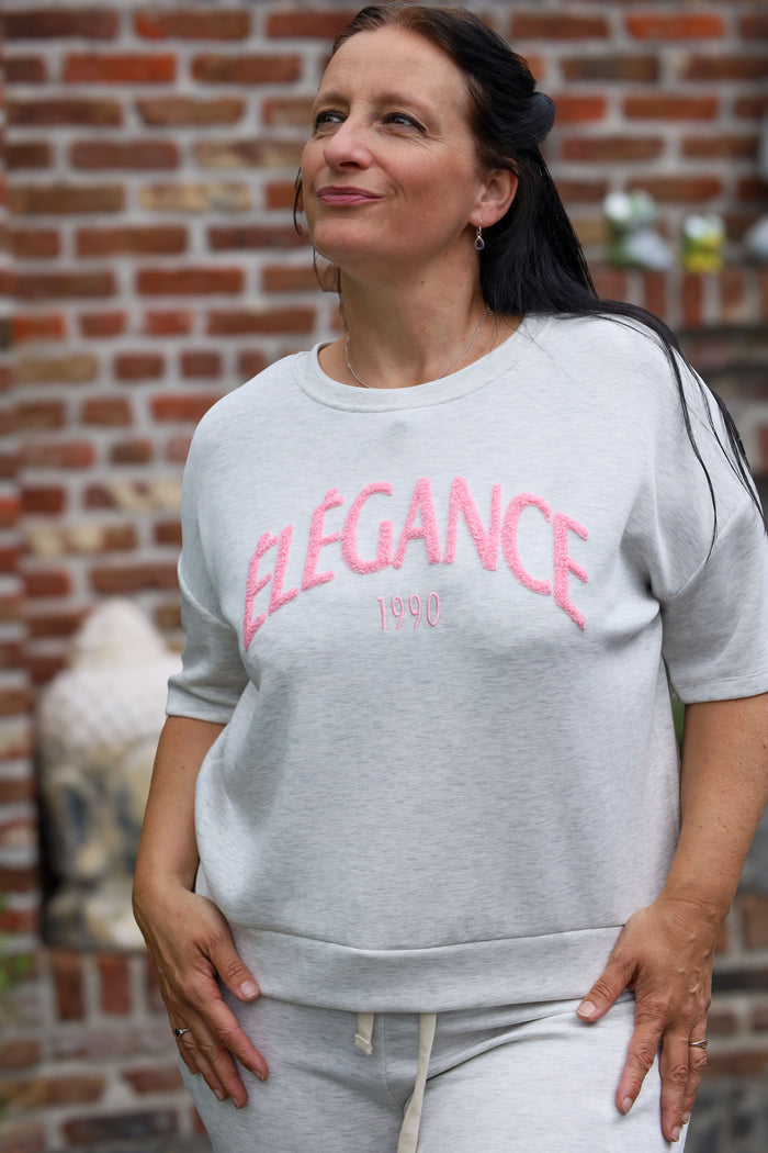 Vrouw draagt lichtgrijze T-shirt “Élégance 1990” uit de La Dolce Vita collectie van She & Me – damesmode Duffel