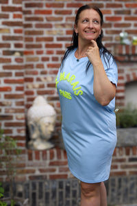 Vrouw in lichtblauwe Mooij jurk met gele 'Le Marais Paris' opdruk – damesmode Duffel